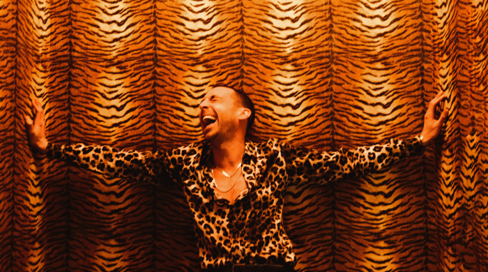 Miles Kane in leopard print shirt standing in front of lion princess backdrop laughing